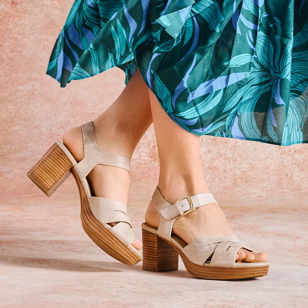 Woman standing in blue dress on beige background featuring the Lacie heel in tan. Shop Heeled sandals.